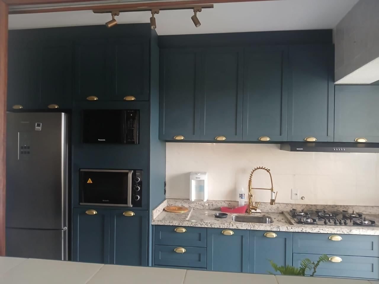 Cozinha planejada com armários verde-petróleo, puxadores dourados, geladeira inox, forno e micro-ondas embutidos