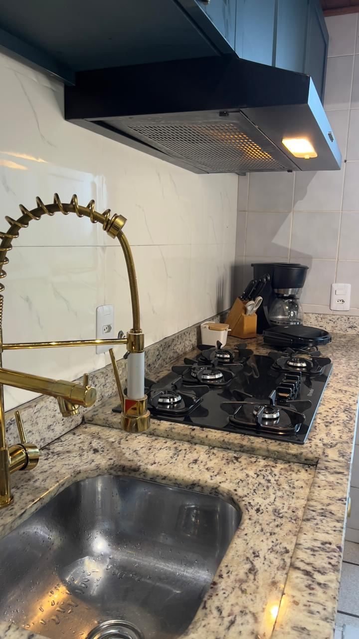 Cooktop de cinco bocas sob coifa preta, com cafeteira e cutelaria na bancada