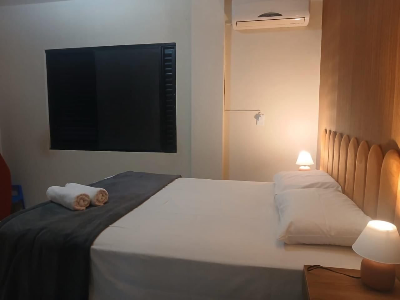 Quarto com cama ampla, cabeceira ripada em madeira clara e ar-condicionado