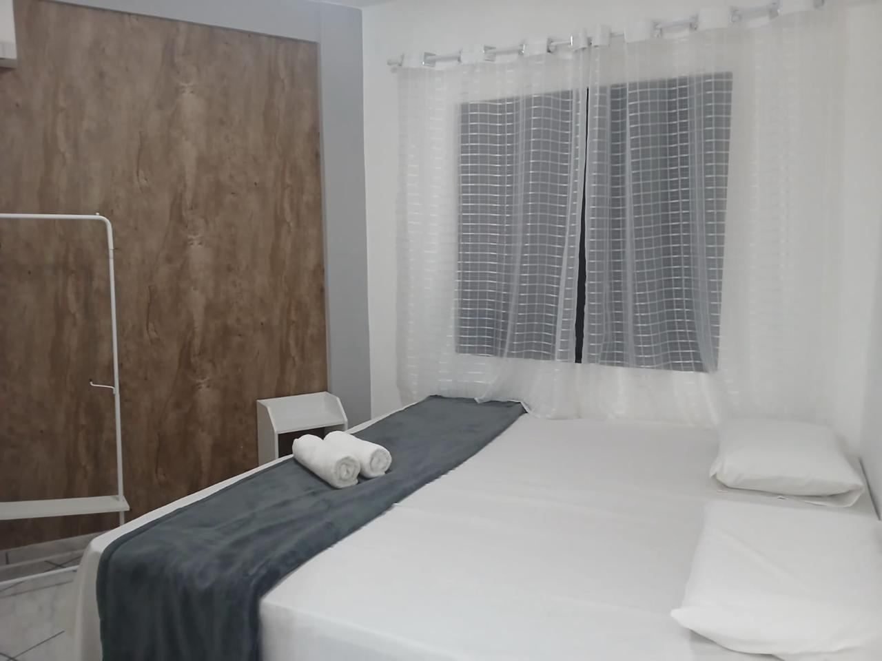 Quarto com cama de casal, painel amadeirado e cortina de voal