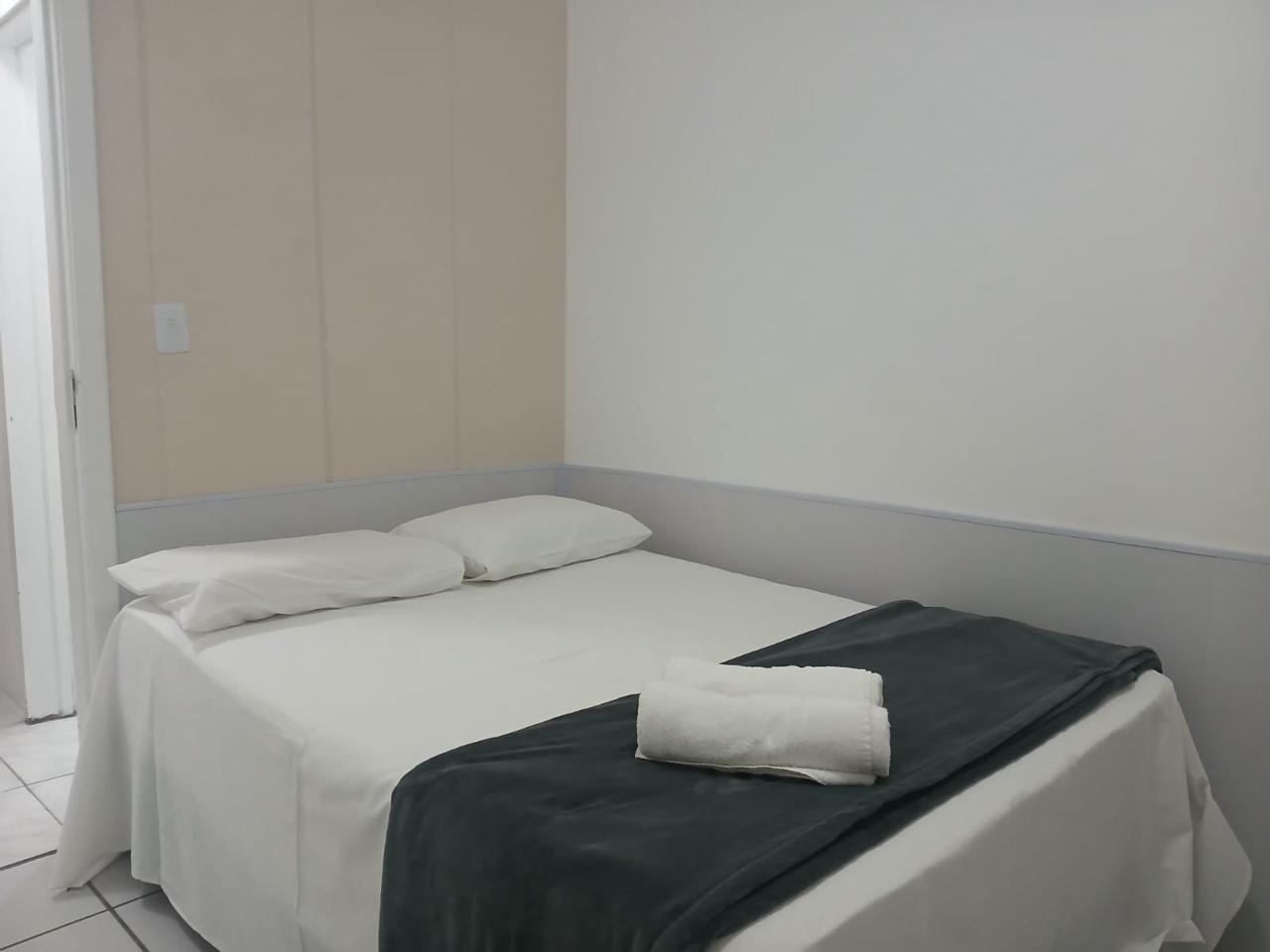 Quarto com cama de casal, painel bege e roupa de cama branca
