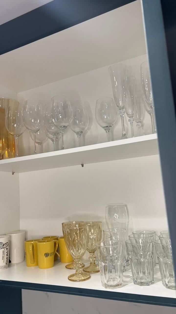 Armário aberto com taças de vinho, copos e canecas organizados