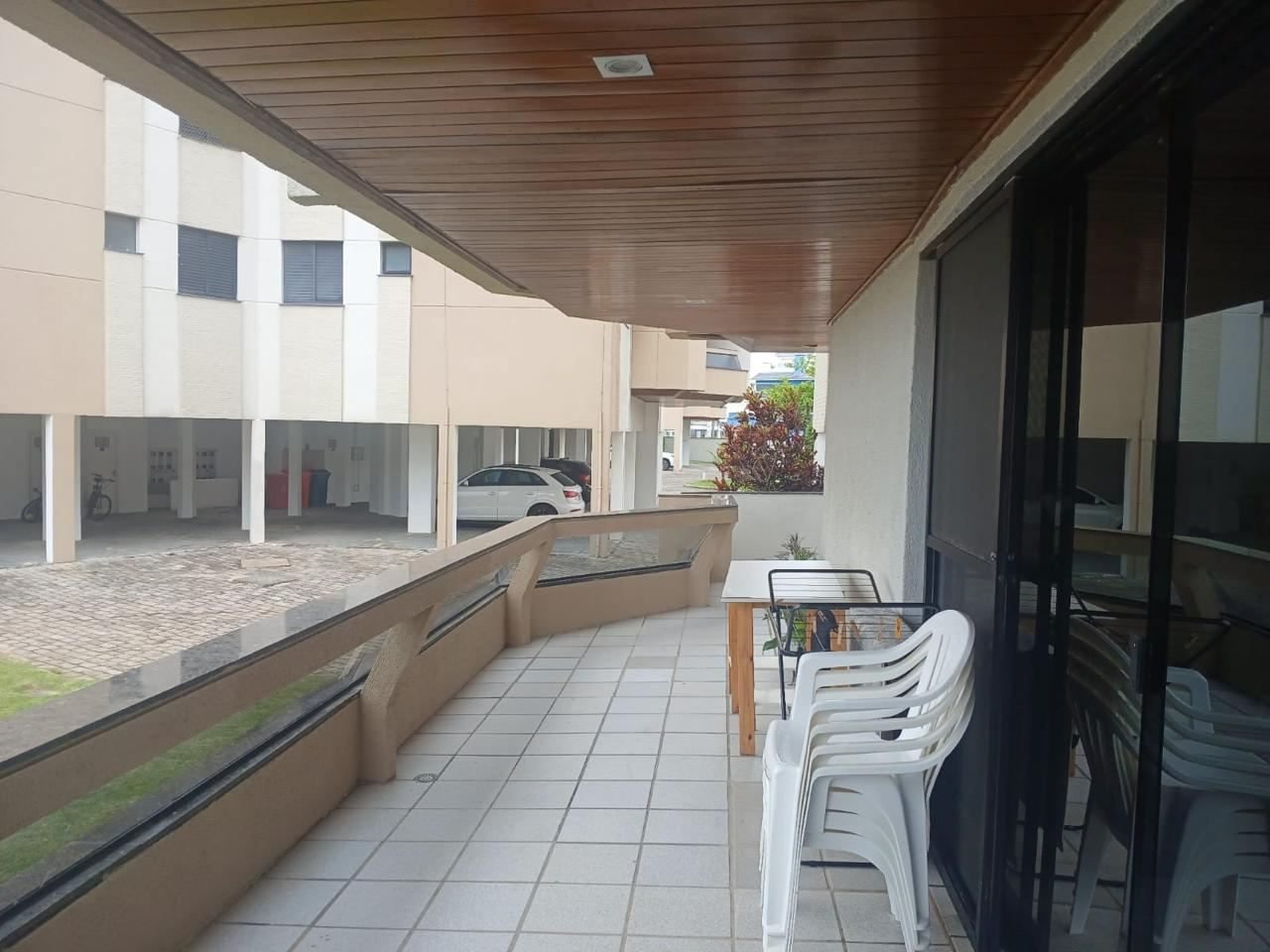 Sacada ampla e coberta com teto de madeira, mesa, cadeiras e acesso ao pátio do condomínio
