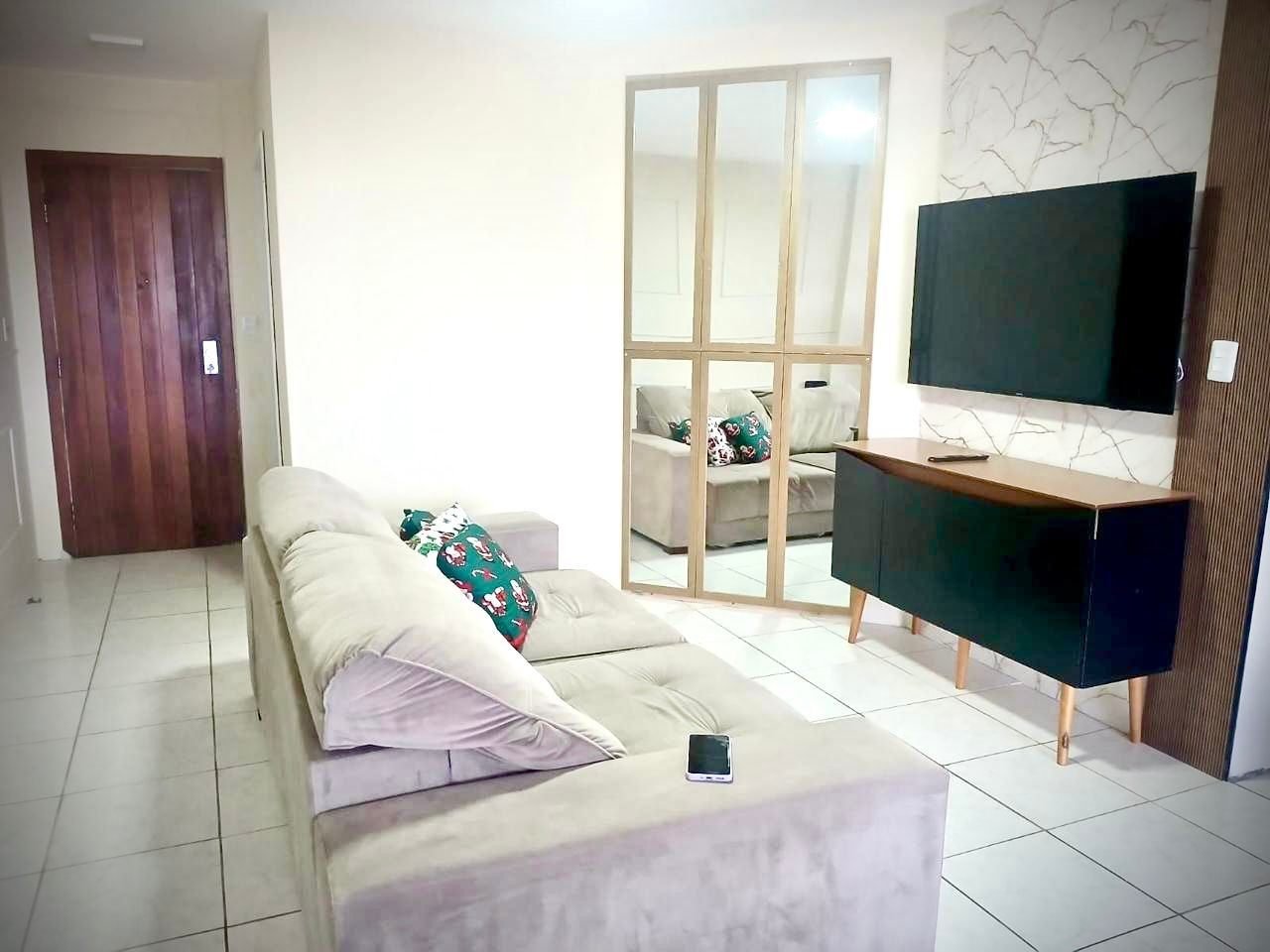 Sala de estar com sofá retrátil bege, Smart TV na parede e buffet de madeira