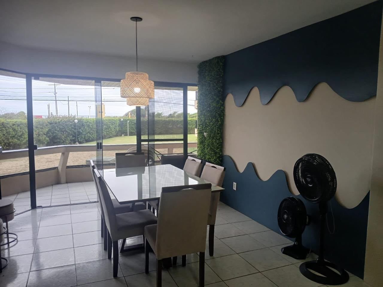 Sala de jantar com mesa de vidro para seis pessoas e portas de vidro abrindo para a sacada, com o mar ao fundo