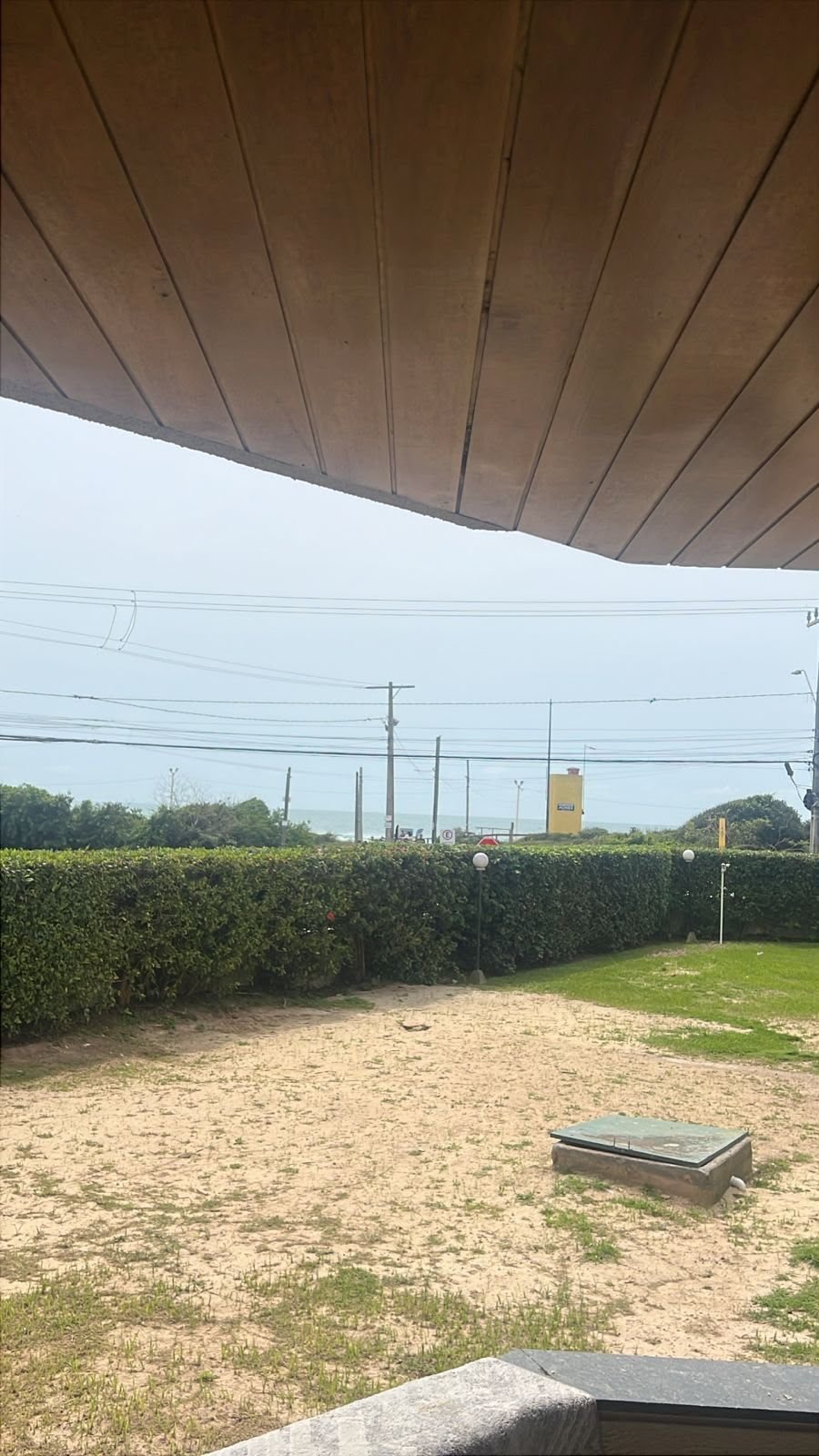 Vista a partir da sacada coberta, com jardim, cerca-viva, a rua e o mar ao fundo